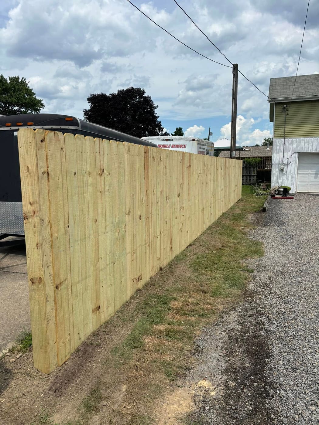 Tall wood privacy fence beside a gravel driveway