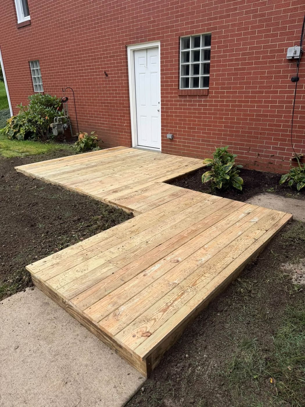 L-shaped pressure-treated walkway deck beside a brick house, view 2